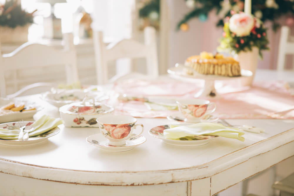 Mesa de chá da tarde simples decorada com xícaras de porcelana, guardanapos de pano, bolo e flores.